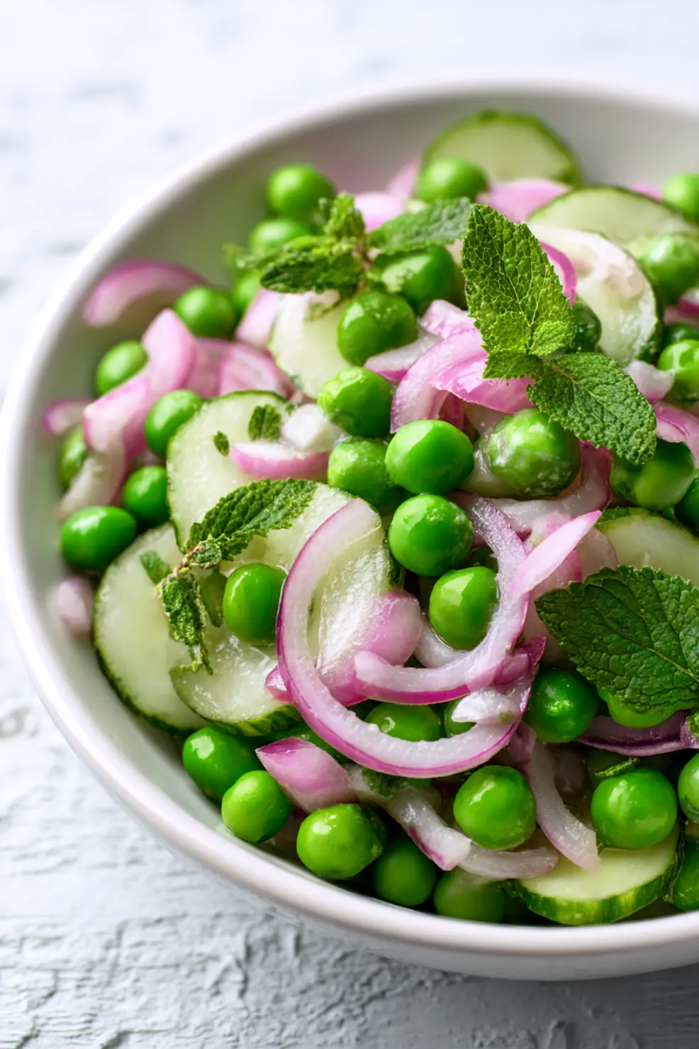 Fresh pea salad recipe in a white bowl showing vibrant green peas, red onions, and herbs