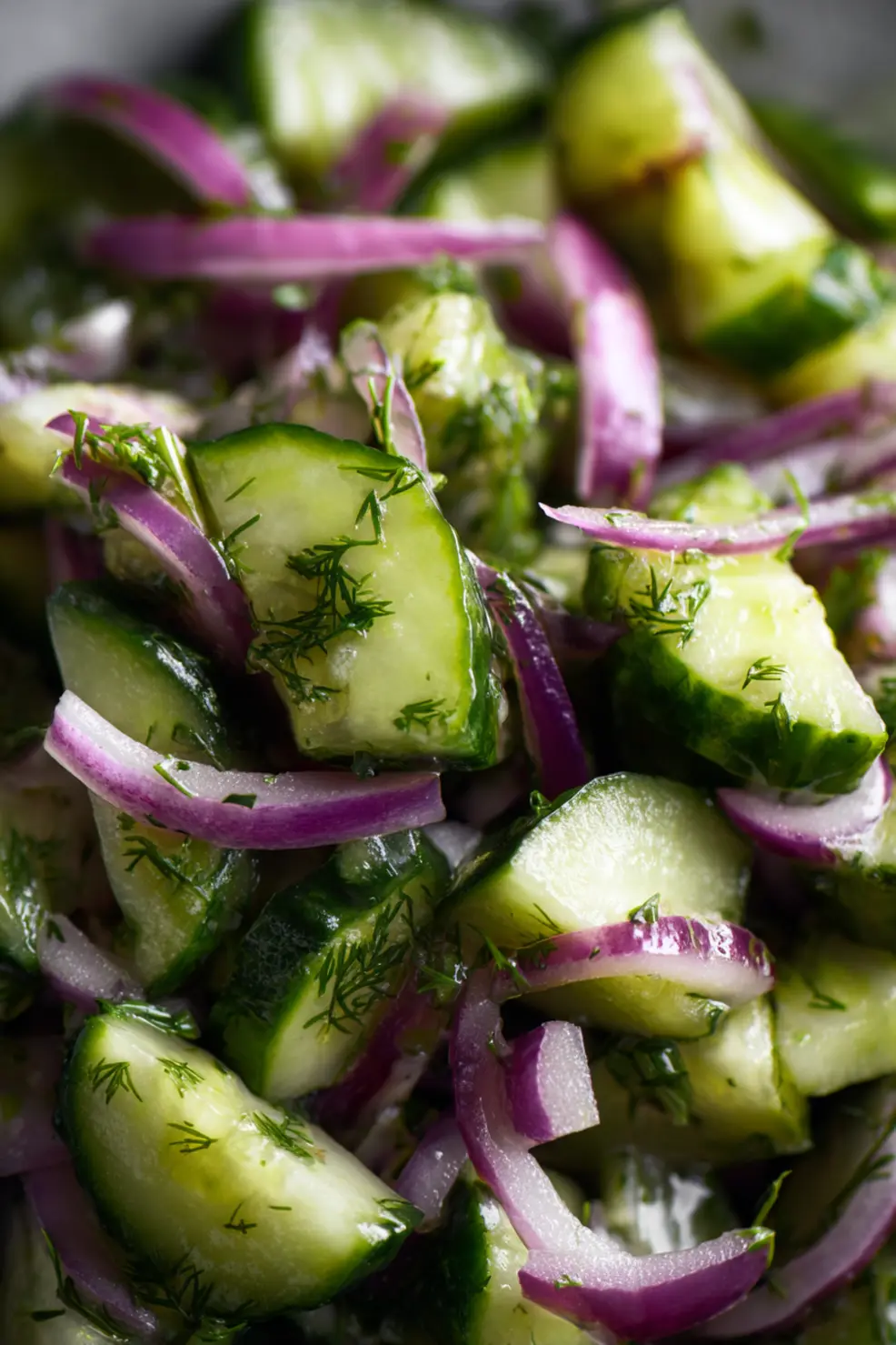 Persian cucumber salad being tossed in a bowl with herbs visible and a lemon wedge on the side