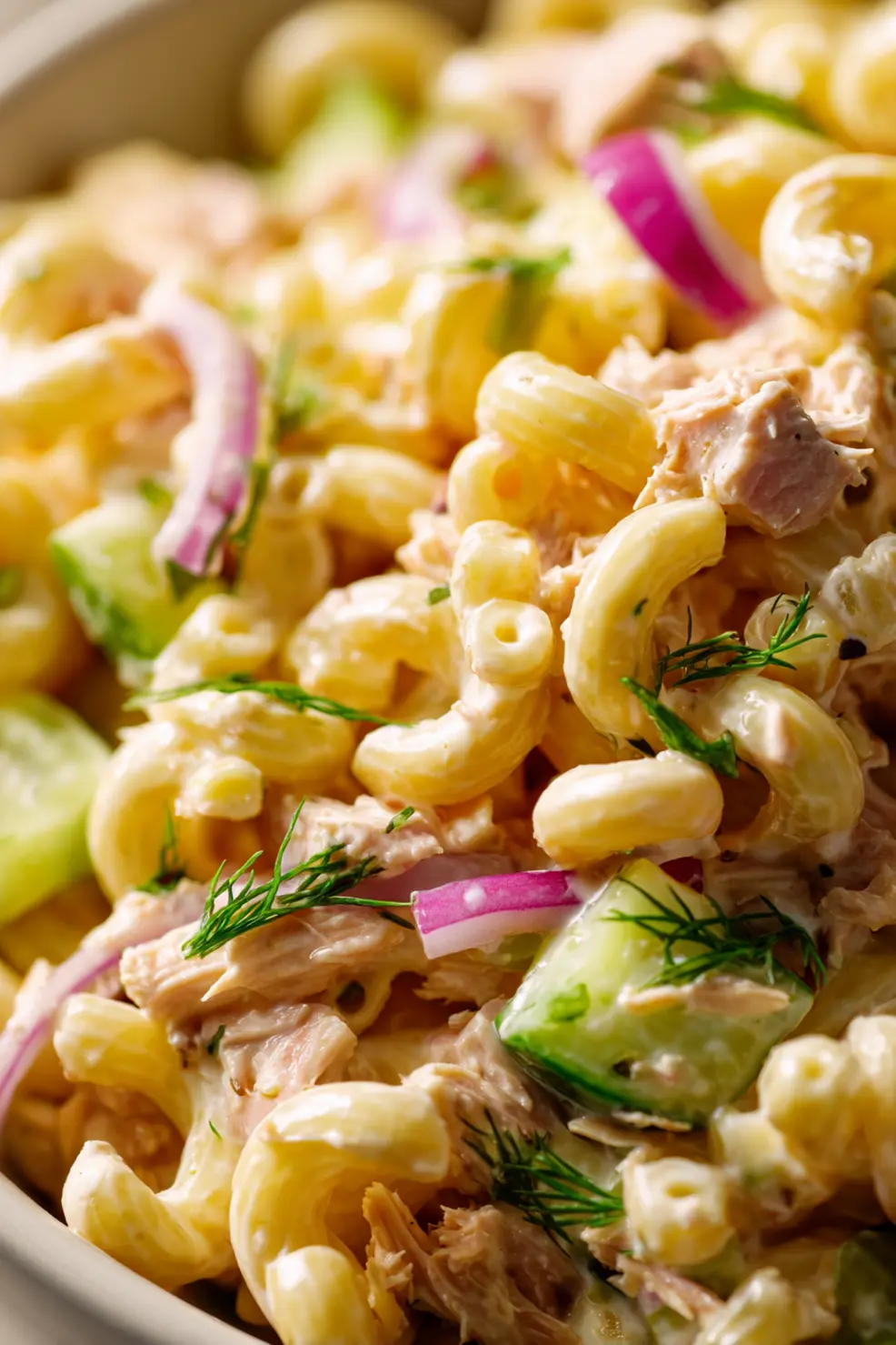 Tuna macaroni salad being served from a large bowl into individual portions, showing the creamy texture and vibrant vegetable pieces mixed with elbow pasta and tuna flakes.