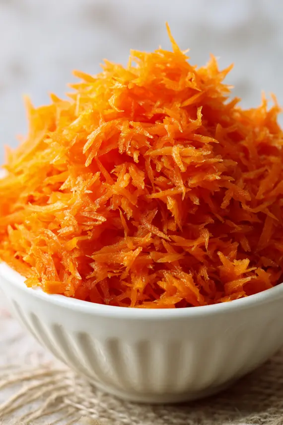 Finished Asian carrot salad in a white serving bowl garnished with sesame seeds and green onions