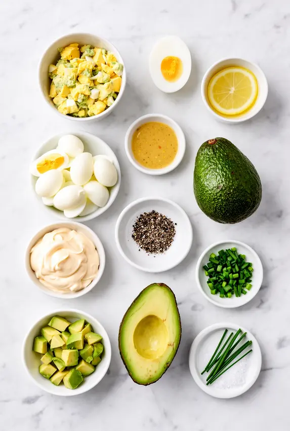 Ingredients laid out for avocado egg salad including eggs, avocado, mayo, mustard, lemon and herbs