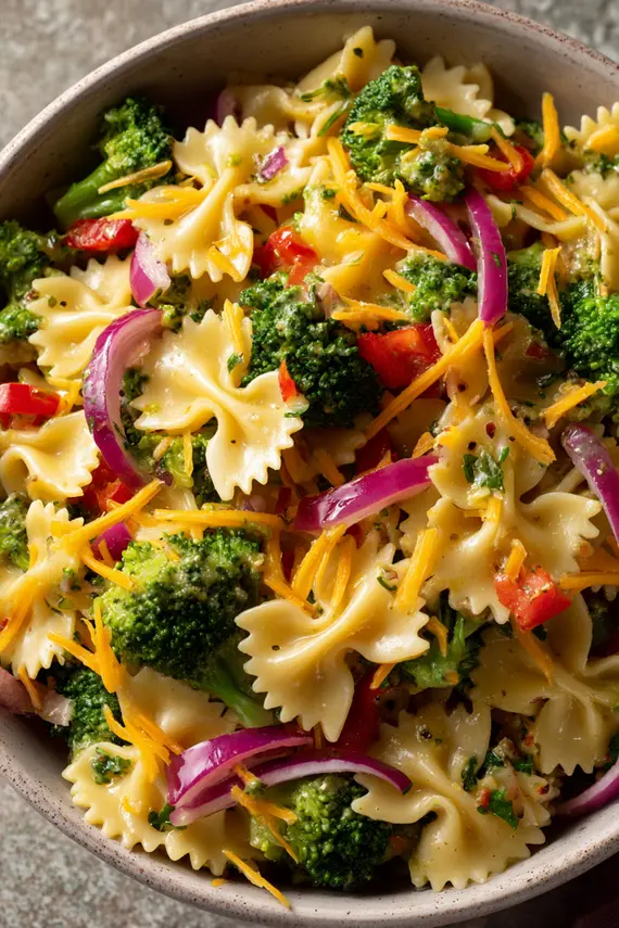 Broccoli pasta salad served in a large white bowl garnished with fresh herbs, showing the vibrant colors of broccoli, red peppers, and pasta