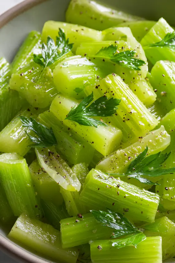 A bowl of fresh celery salad with parsley garnish served on a wooden table with lemon wedges on the side
