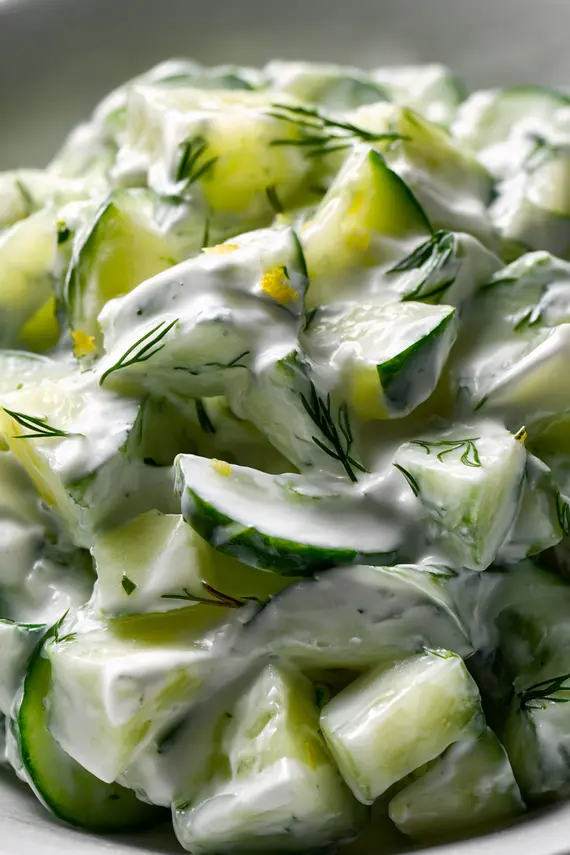 Finished cucumber yogurt salad garnished with fresh herbs in a white bowl