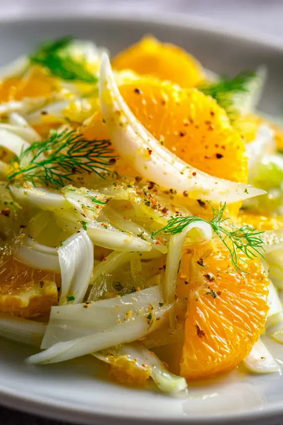 Finished fennel and orange salad served in a white bowl, showcasing the bright orange segments contrasting with the pale fennel slices, garnished with herbs and pine nuts