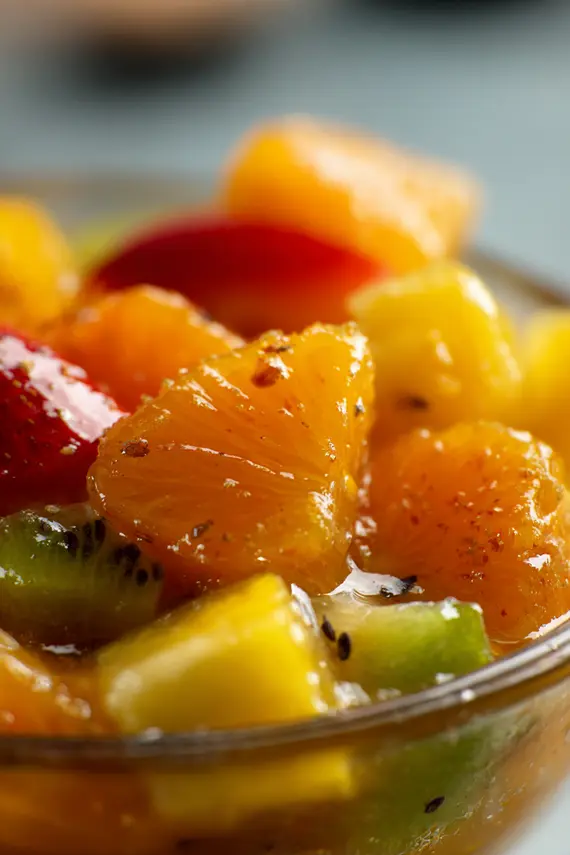 Homemade citrus-ginger fruit salad dressing being drizzled over a colorful bowl of mixed fresh fruits