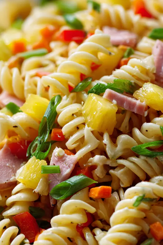 Hawaiian pasta salad served in a large white bowl garnished with green onions and a pineapple wedge on a tropical-themed table setting