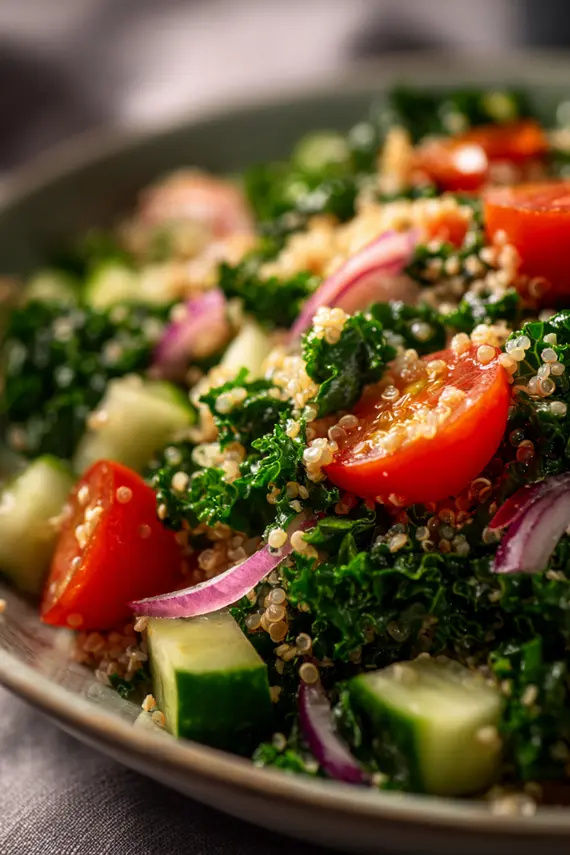 Kale and quinoa salad in a white bowl with ingredients surrounding it