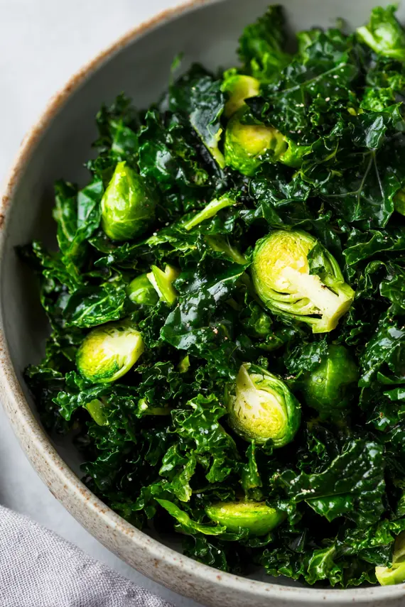 Beautifully plated kale brussel sprout salad in a serving bowl garnished with pumpkin seeds