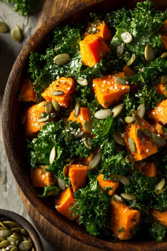 Kale sweet potato salad in a white bowl garnished with pumpkin seeds