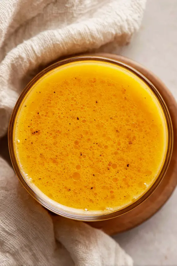Orange salad dressing in a glass jar with fresh oranges and salad ingredients nearby