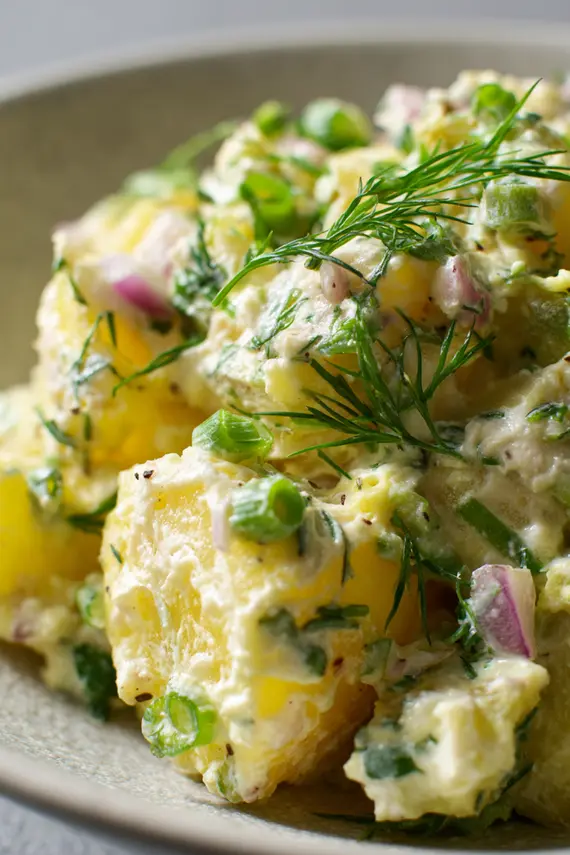 Finished potato salad without mayo garnished with herbs in a white serving bowl