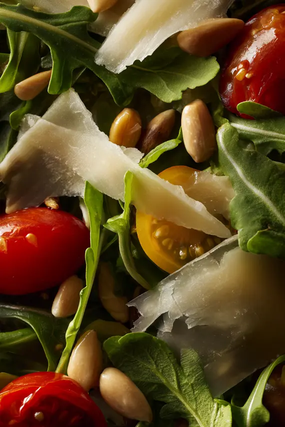 Close-up of rocket salad with parmesan shavings and cherry tomatoes on a black plate